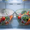 Fresh vegetables and produce in glass bowls wrapped in anti-fog light green PVC film inside a refrigerator