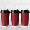 Wholesale black and maroon double wall ripple paper coffee cups with lids on a white wooden background